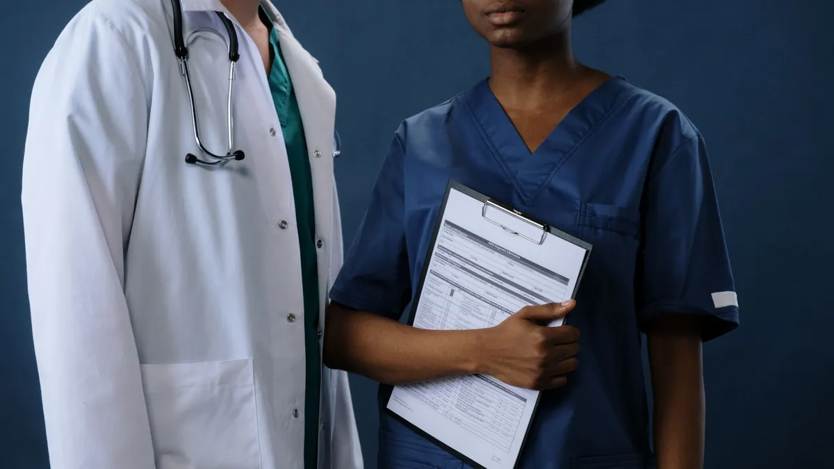 Two healthcare professionals in scrubs and lab coat with a clipboard, representing teamwork.