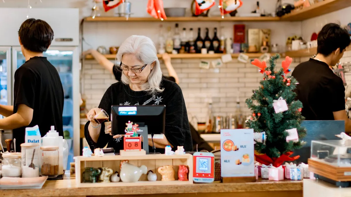Elderly woman managing a festive cafe counter during Christmas season.
