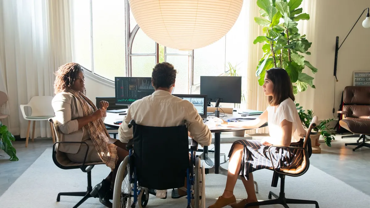 Diverse team having a discussion in a modern office setting with natural light. Includes a member using a wheelchair.