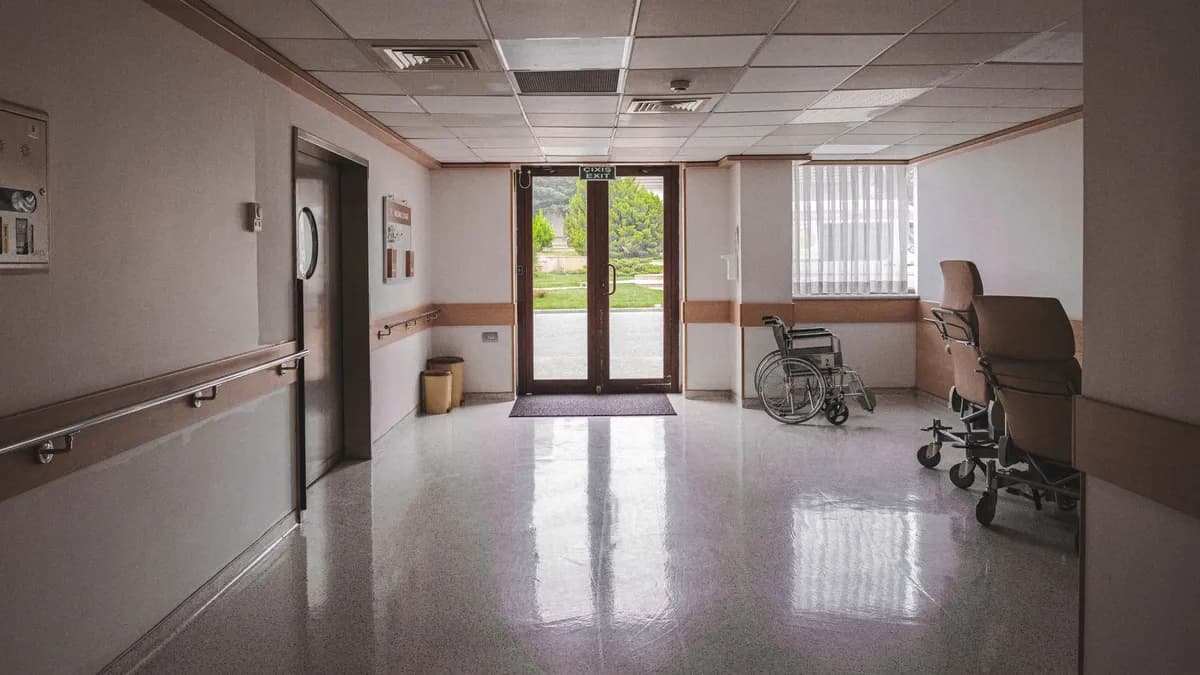 Hospital corridor with wheelchair, reflecting glass doors, and outdoor view. Ideal for healthcare themes.