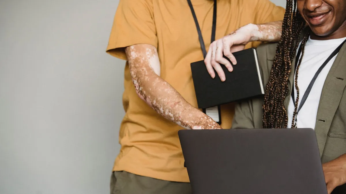 Unrecognizable African American male with Afro braids and black coworker with vitiligo and notebook surfing computer on gray background in studio
