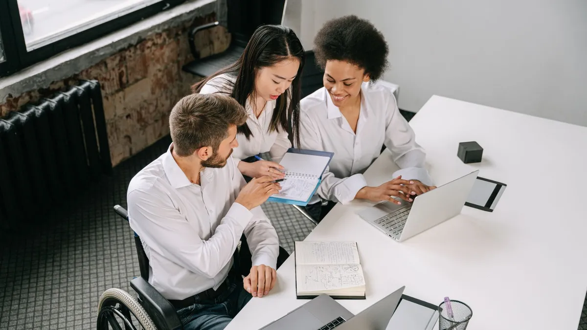 Three colleagues collaborating around a desk in an office space, showcasing diversity and teamwork.