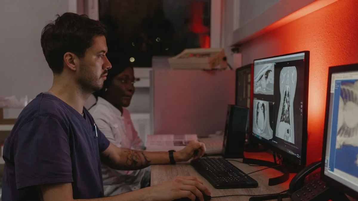 Two healthcare professionals working at computers analyzing medical scans in a clinical setting.