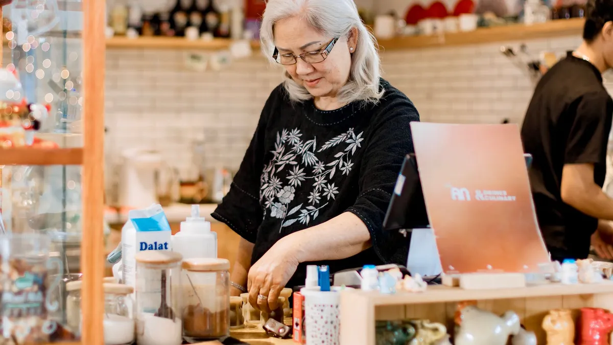 Senior woman working behind the counter in a cozy, warmly lit coffee shop.