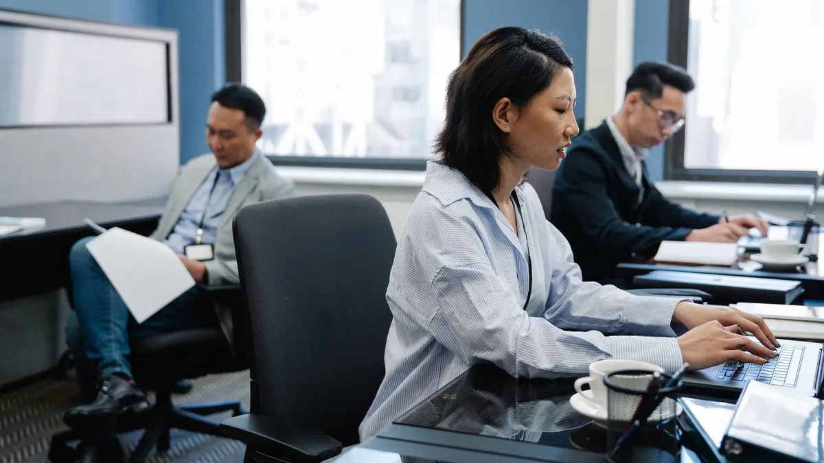 Focused Asian professionals working on laptops in a modern office environment, emphasizing collaboration.